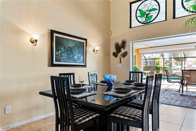 dining space featuring light tile patterned floors, a high ceiling, a sunroom, and baseboards