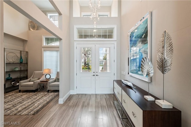 entryway featuring a high ceiling, an inviting chandelier, light hardwood / wood-style floors, and french doors