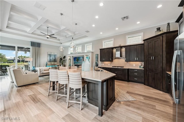 kitchen with wall chimney exhaust hood, sink, a breakfast bar area, hanging light fixtures, and a large island