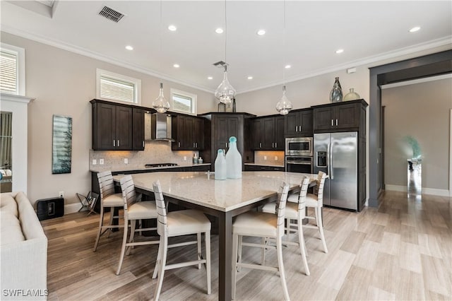 kitchen featuring dark brown cabinetry, wall chimney exhaust hood, decorative light fixtures, appliances with stainless steel finishes, and a large island