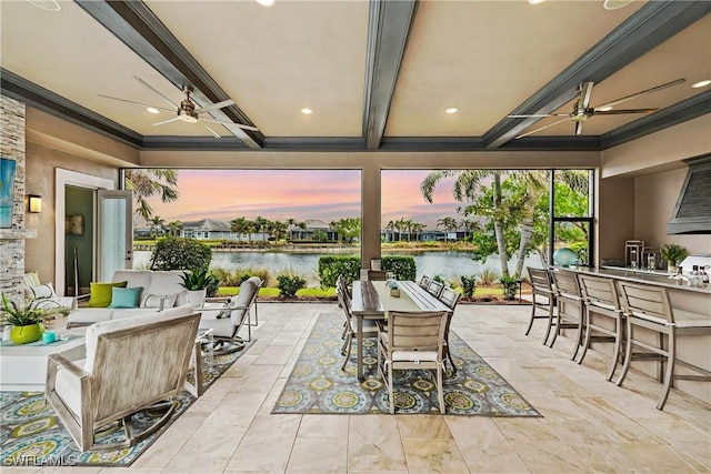 patio terrace at dusk featuring an outdoor bar, ceiling fan, and a water view