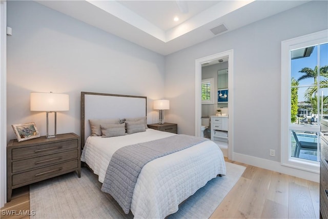 bedroom with multiple windows, ensuite bath, and light hardwood / wood-style floors