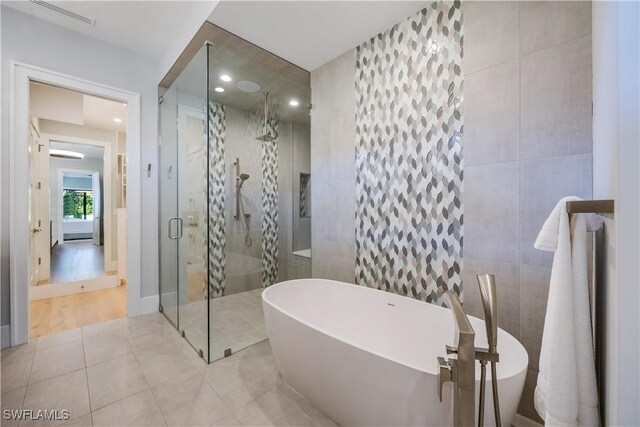 bathroom featuring independent shower and bath, tile patterned flooring, and tile walls