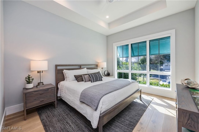 bedroom featuring a tray ceiling, light wood-style flooring, baseboards, and recessed lighting