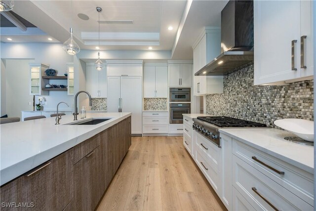 kitchen featuring wall chimney range hood, white cabinetry, a tray ceiling, decorative light fixtures, and stainless steel gas stovetop