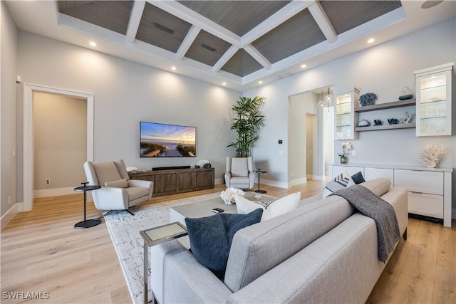 living room with a towering ceiling, light wood-style floors, visible vents, and coffered ceiling