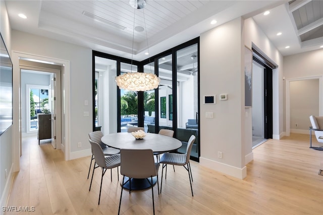 dining space with a tray ceiling, light wood-type flooring, and baseboards