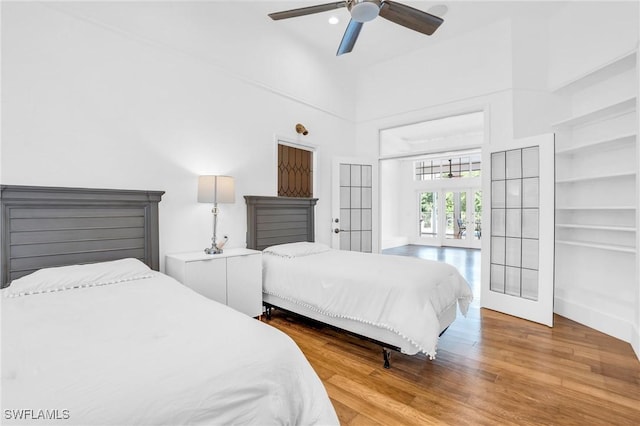 bedroom featuring a towering ceiling, a ceiling fan, wood finished floors, and french doors