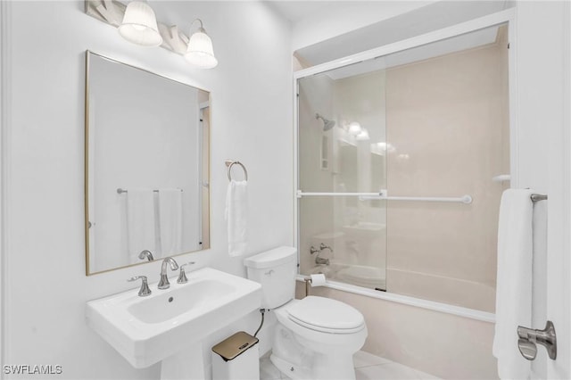 bathroom featuring toilet, bath / shower combo with glass door, and a sink