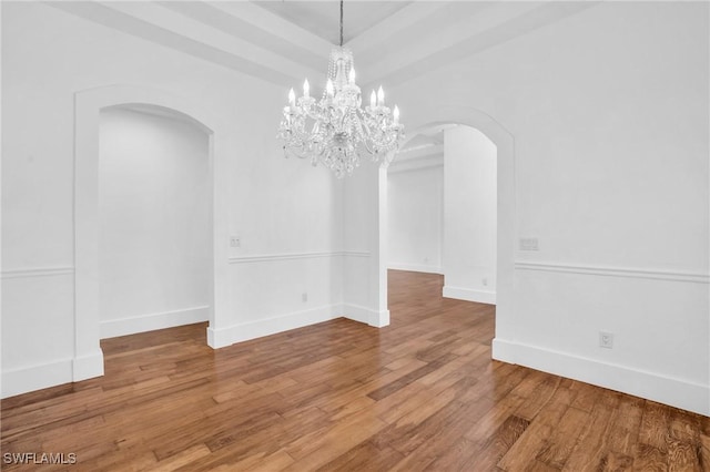 unfurnished dining area with arched walkways, baseboards, and hardwood / wood-style flooring