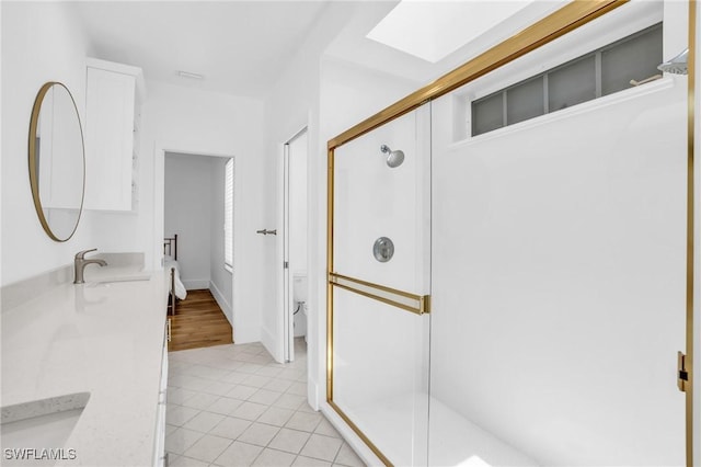 full bathroom featuring a stall shower, a skylight, toilet, tile patterned floors, and vanity