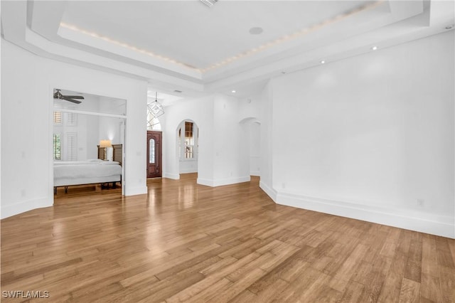 empty room with light wood finished floors, a tray ceiling, and arched walkways