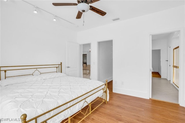 bedroom with rail lighting, visible vents, a ceiling fan, wood finished floors, and baseboards