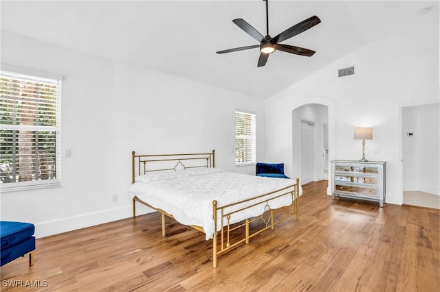 bedroom featuring arched walkways, wood finished floors, visible vents, baseboards, and vaulted ceiling