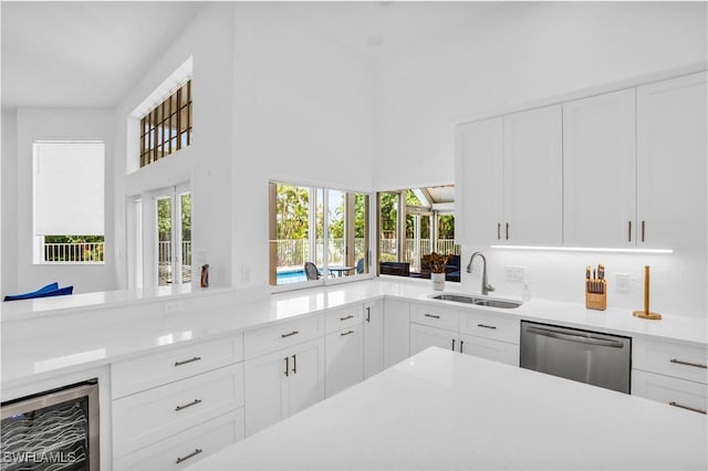 kitchen with wine cooler, light countertops, stainless steel dishwasher, white cabinetry, and a sink