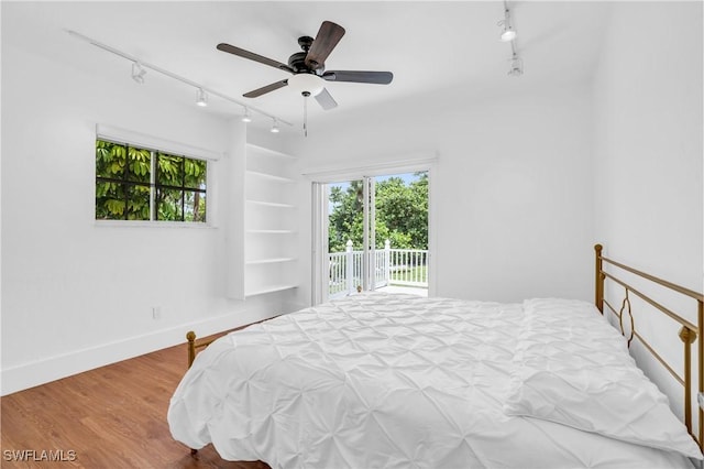 bedroom featuring access to outside, multiple windows, baseboards, and wood finished floors