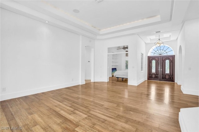 entryway with light wood-style floors, arched walkways, and a raised ceiling