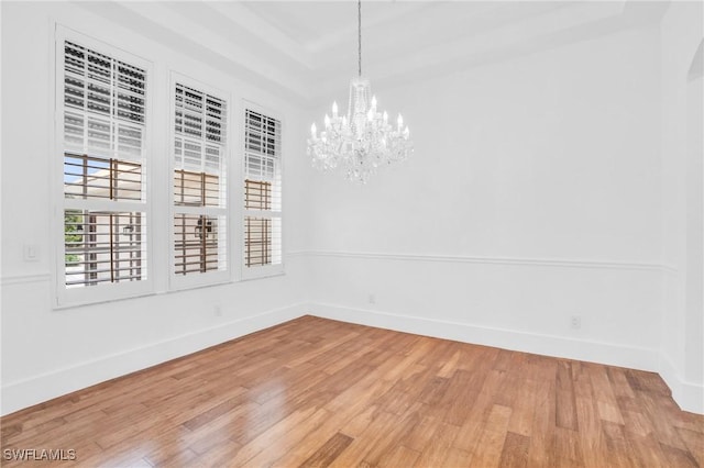 spare room featuring a tray ceiling, light wood-type flooring, an inviting chandelier, and baseboards