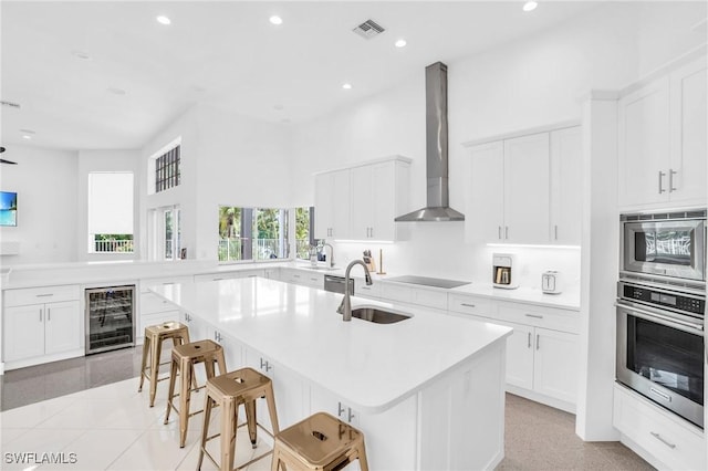 kitchen featuring beverage cooler, a sink, visible vents, appliances with stainless steel finishes, and wall chimney range hood