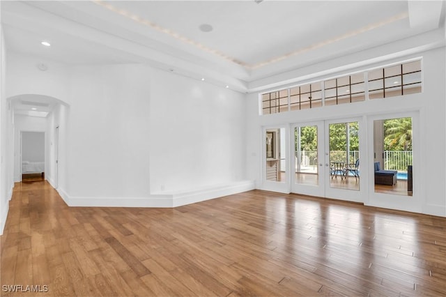 unfurnished room with arched walkways, french doors, a raised ceiling, wood finished floors, and baseboards