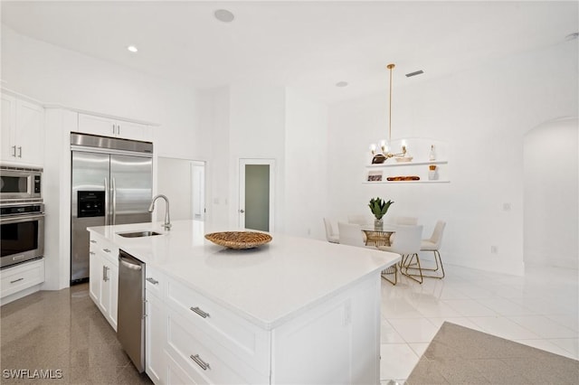 4090 W Gulf Dr, Sanibel, FL 33957 - kitchen featuring an inviting chandelier, a kitchen island with sink, a sink, built in appliances, and white cabinetry