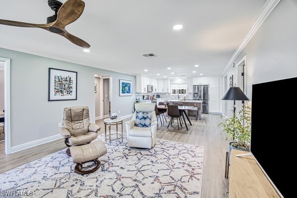 living room with ceiling fan, ornamental molding, and light hardwood / wood-style floors