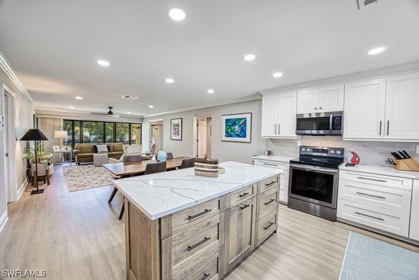 kitchen with crown molding, white cabinetry, stainless steel appliances, light stone counters, and a kitchen island