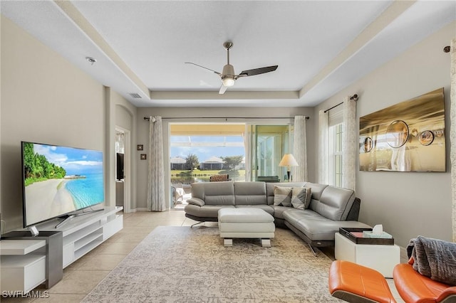 tiled living room with ceiling fan and a raised ceiling