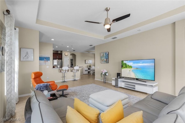 living room with light tile patterned floors, a raised ceiling, and ceiling fan