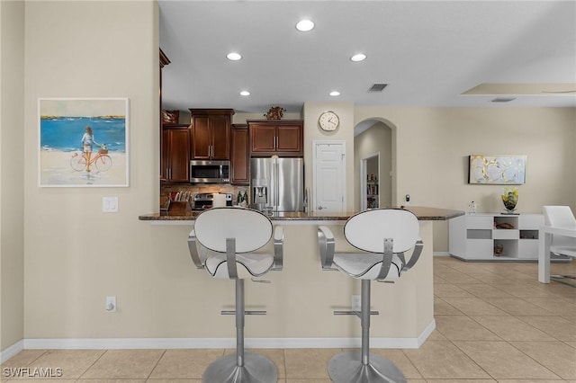 kitchen featuring light tile patterned flooring, a breakfast bar, tasteful backsplash, appliances with stainless steel finishes, and dark stone counters