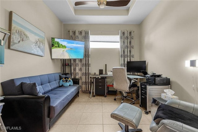 home office with light tile patterned flooring, ceiling fan, and a raised ceiling