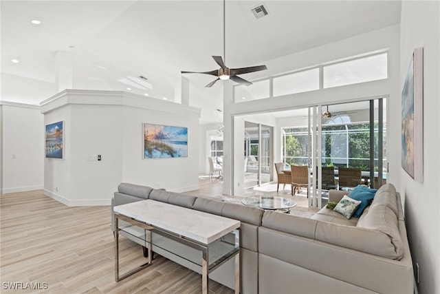 living room with a high ceiling, ceiling fan, and light hardwood / wood-style flooring