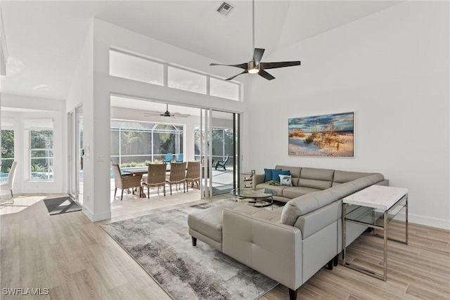 living room featuring a high ceiling, ceiling fan, and light hardwood / wood-style floors