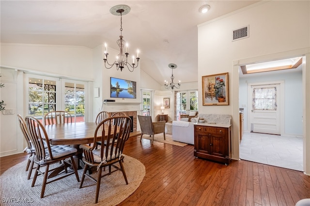 dining room featuring hardwood / wood-style floors, high vaulted ceiling, a fireplace, a chandelier, and french doors