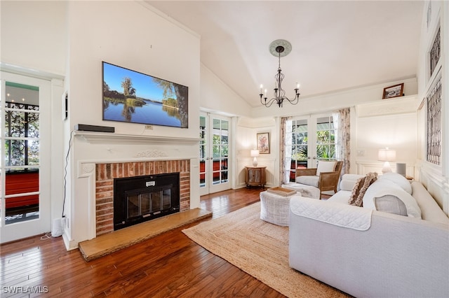 living room featuring high vaulted ceiling, a chandelier, hardwood / wood-style flooring, a brick fireplace, and french doors