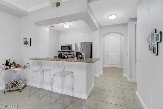 kitchen with light tile patterned flooring, stone countertops, appliances with stainless steel finishes, kitchen peninsula, and white cabinets