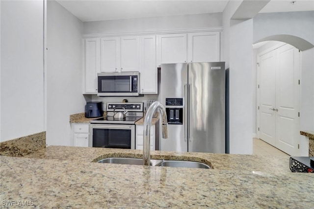 kitchen with stainless steel appliances, sink, white cabinets, and light stone counters