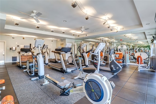 gym featuring track lighting, ceiling fan, and a tray ceiling