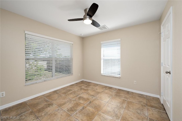 spare room with stone finish floor, visible vents, baseboards, and a ceiling fan