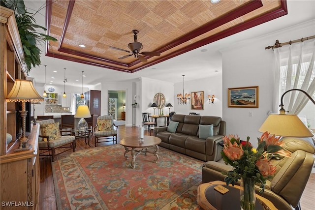 living room featuring crown molding, hardwood / wood-style floors, a tray ceiling, and ceiling fan with notable chandelier