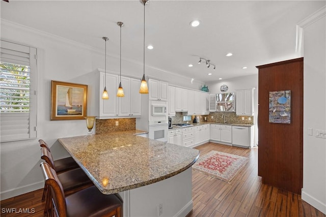 kitchen featuring a breakfast bar, decorative light fixtures, kitchen peninsula, white appliances, and white cabinets