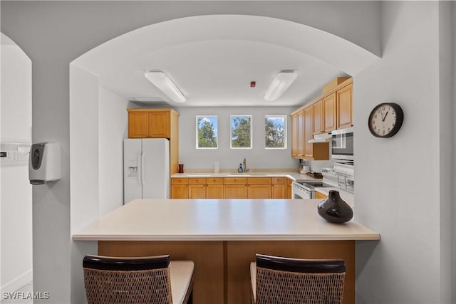 kitchen with light brown cabinetry, sink, white appliances, and kitchen peninsula