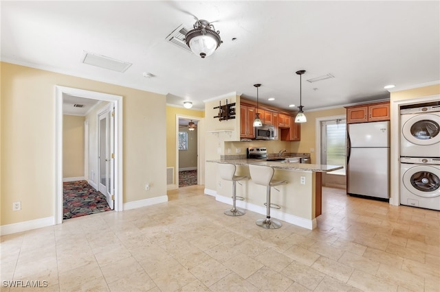 kitchen featuring brown cabinetry, stacked washer / dryer, light stone counters, a peninsula, and stainless steel appliances