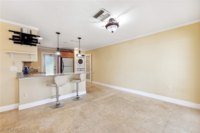 kitchen with visible vents, ornamental molding, freestanding refrigerator, stacked washing maching and dryer, and baseboards