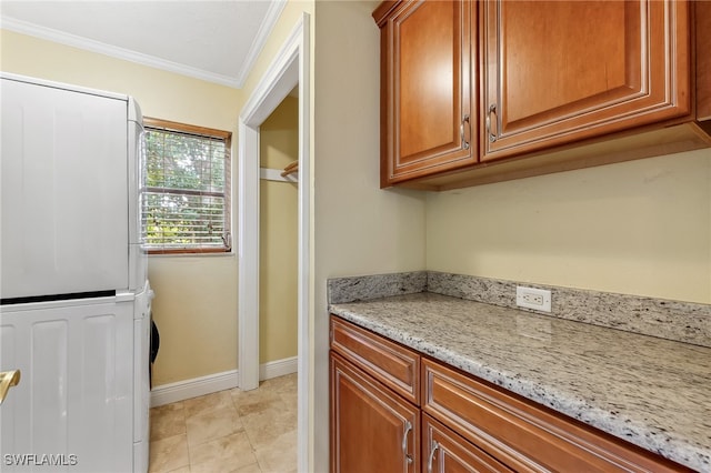 interior space featuring light tile patterned floors, light stone countertops, stacked washer / drying machine, brown cabinets, and crown molding