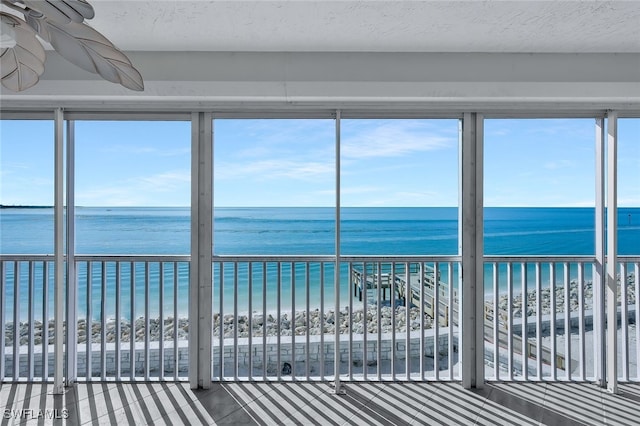 unfurnished sunroom with a healthy amount of sunlight, a beach view, and a water view