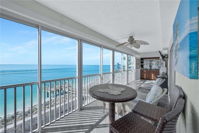 sunroom / solarium with a water view, ceiling fan, and a view of the beach