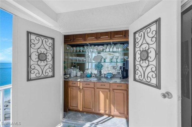 bar with a water view, tile patterned floors, and dark stone countertops