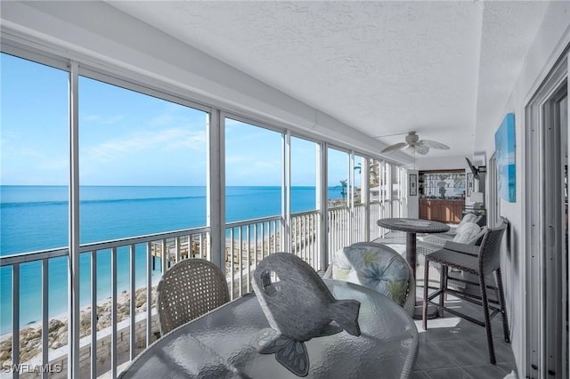 sunroom featuring a water view, ceiling fan, and a beach view