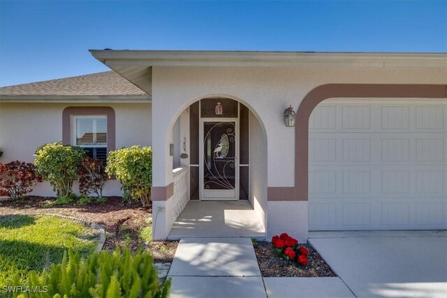 entrance to property with roof with shingles, an attached garage, and stucco siding